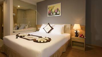 A neatly made bed with a decorative pillow, a bedside table with a lamp and fruit, and a large mirror reflecting the room.