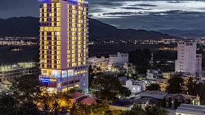 A tall hotel with multiple floors, a prominent sign reading "Dendro Gold," and a view of surrounding buildings and mountains. - Dendro Gold Hotel (Nha Trang)
