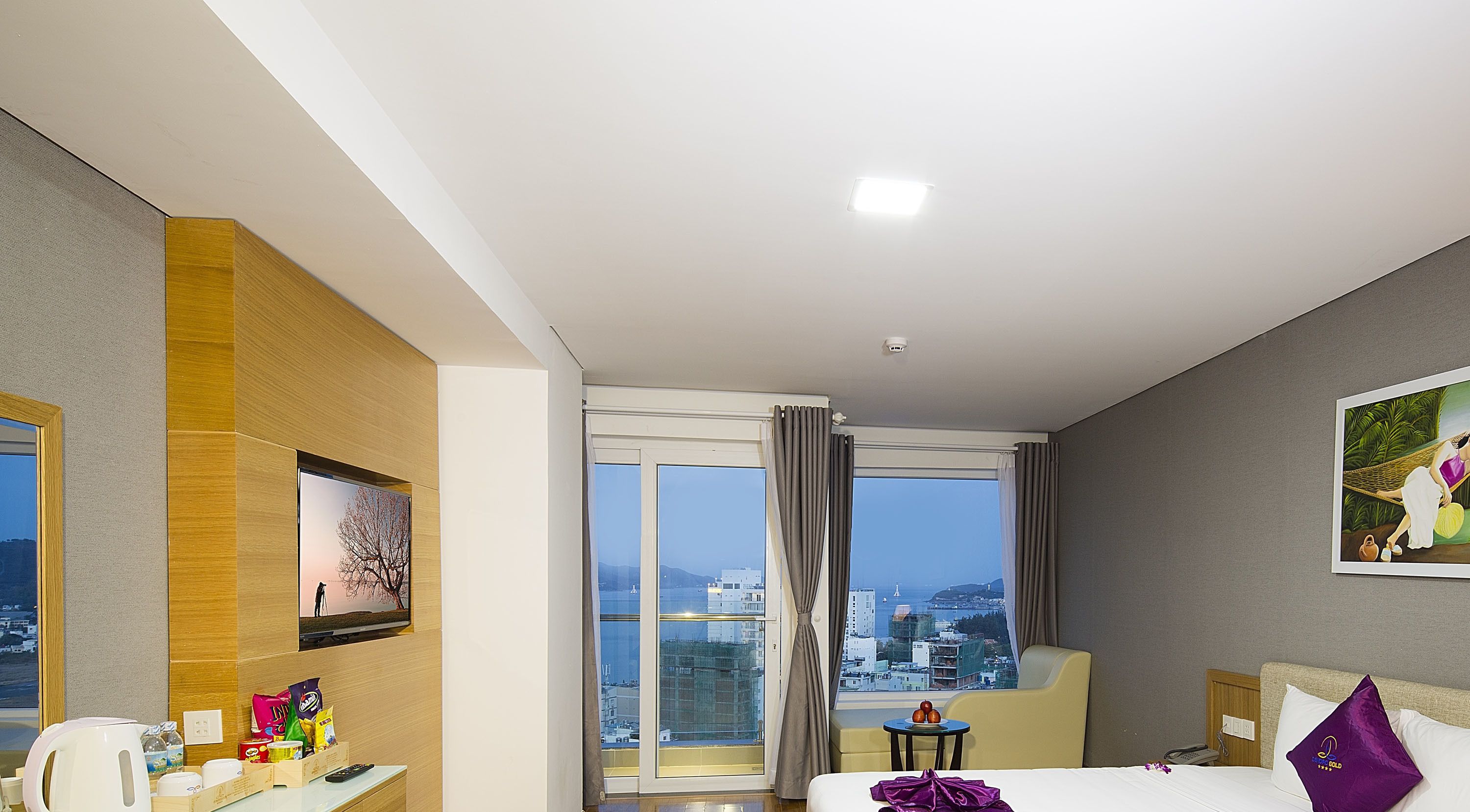 Une chambre d’hôtel avec une grande fenêtre, un lit, un bureau avec un ordinateur et une vue sur la ville.