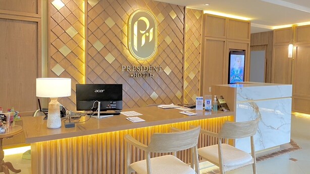A hotel reception desk with a modern design, featuring a logo, a computer, and a television. - President Hotel (Udon Thani)