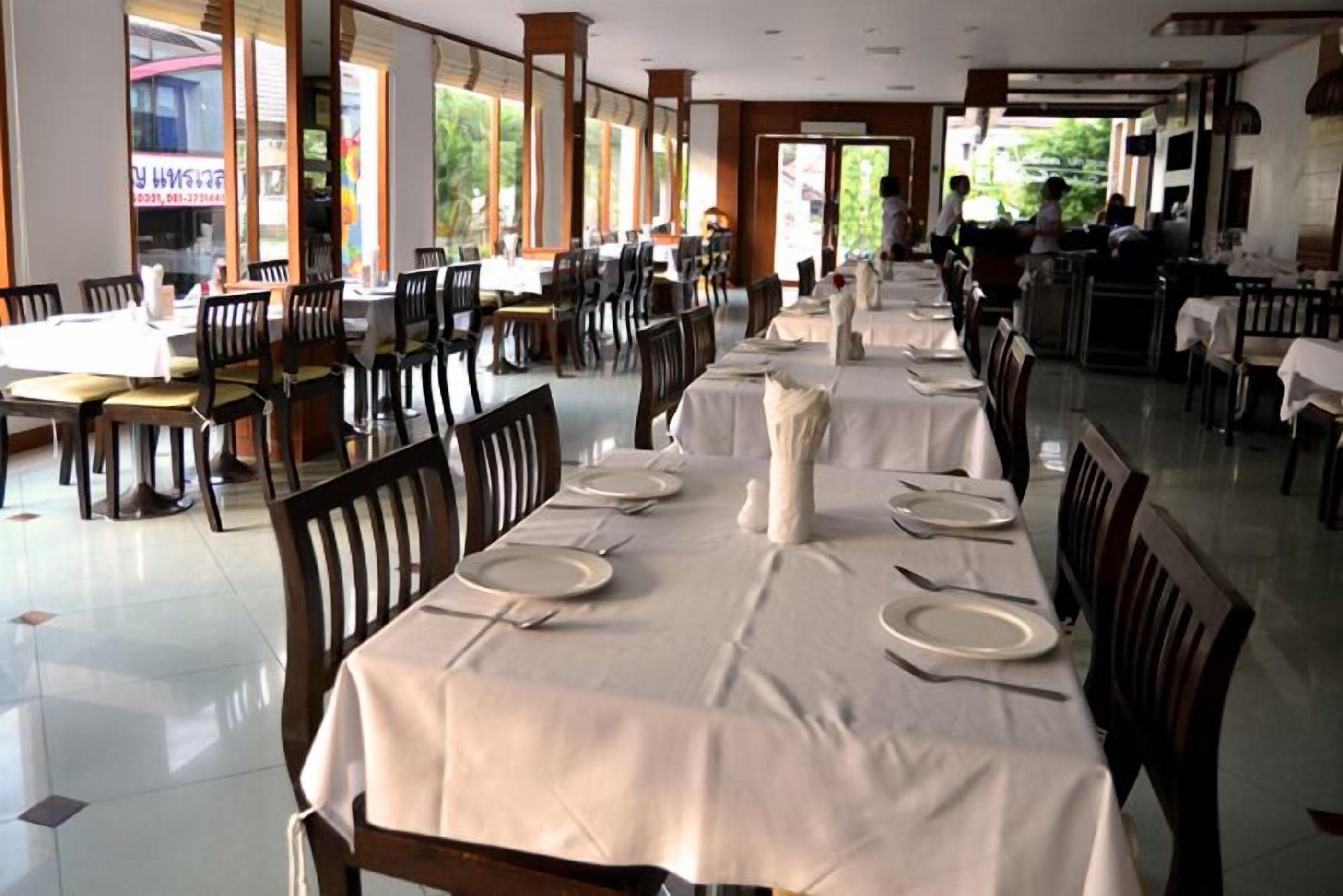 A spacious dining area with multiple tables set for service, large windows, and a view of the outdoors.