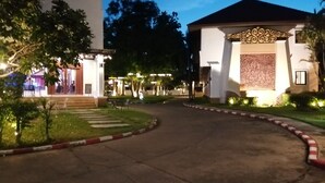 A well-lit hotel entrance with a curved driveway, a small lawn, and a decorative wall with intricate patterns. - President Hotel (Udon Thani)