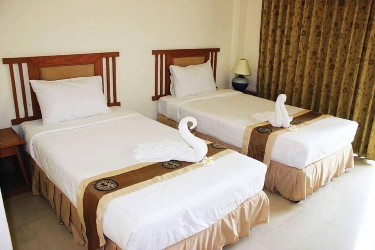 Quarto de hotel com duas camas, cada uma com cabeceira de madeira, roupa de cama branca e almofadas decorativas em formato de cisne.