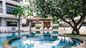 A swimming pool with a tiled edge, surrounded by white lounge chairs and a palm tree. - President Hotel (Udon Thani)