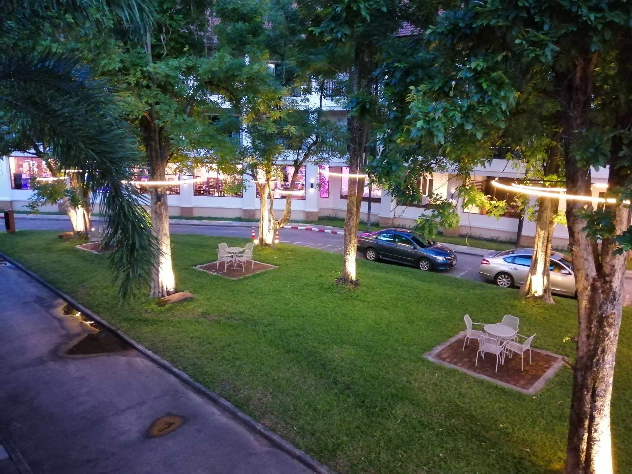 A well-maintained outdoor area with neatly trimmed grass, several trees, and outdoor seating arrangements.