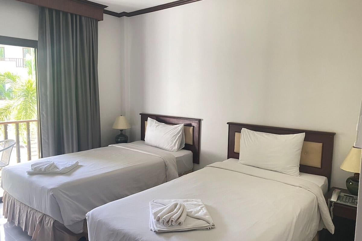Quarto de hotel com duas camas, uma varanda e uma mesinha com abajur.