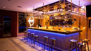 A bar area with a counter, stools, and shelves of bottles. - President Hotel (Udon Thani)