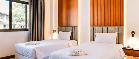 A hotel room with two beds, a window with curtains, wooden paneling on the walls, and a nightstand with a lamp.