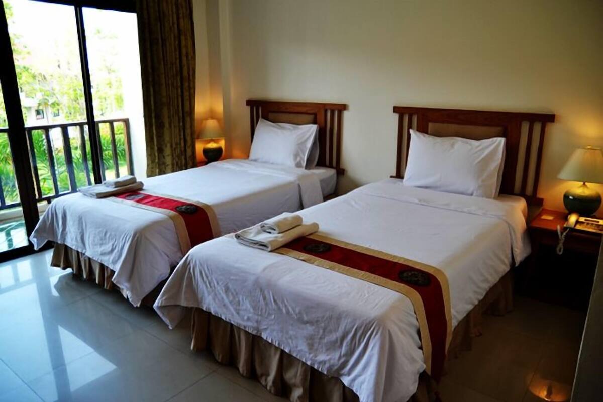 Quarto de hotel com duas camas, uma varanda e uma mesa de cabeceira com abajur.