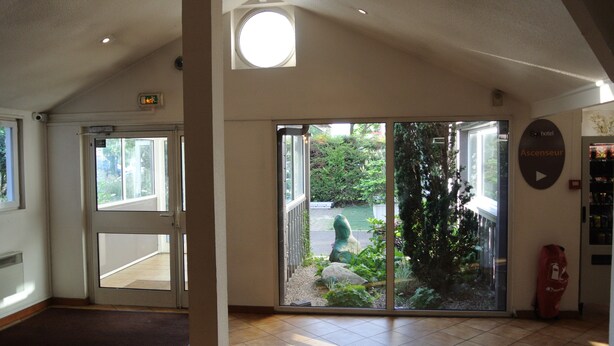 L’entrée d’un hôtel, avec une porte vitrée donnant sur un jardin.