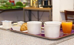 Una bandeja de desayuno con cruasanes, yogur y jugo de naranja sobre una mesa.