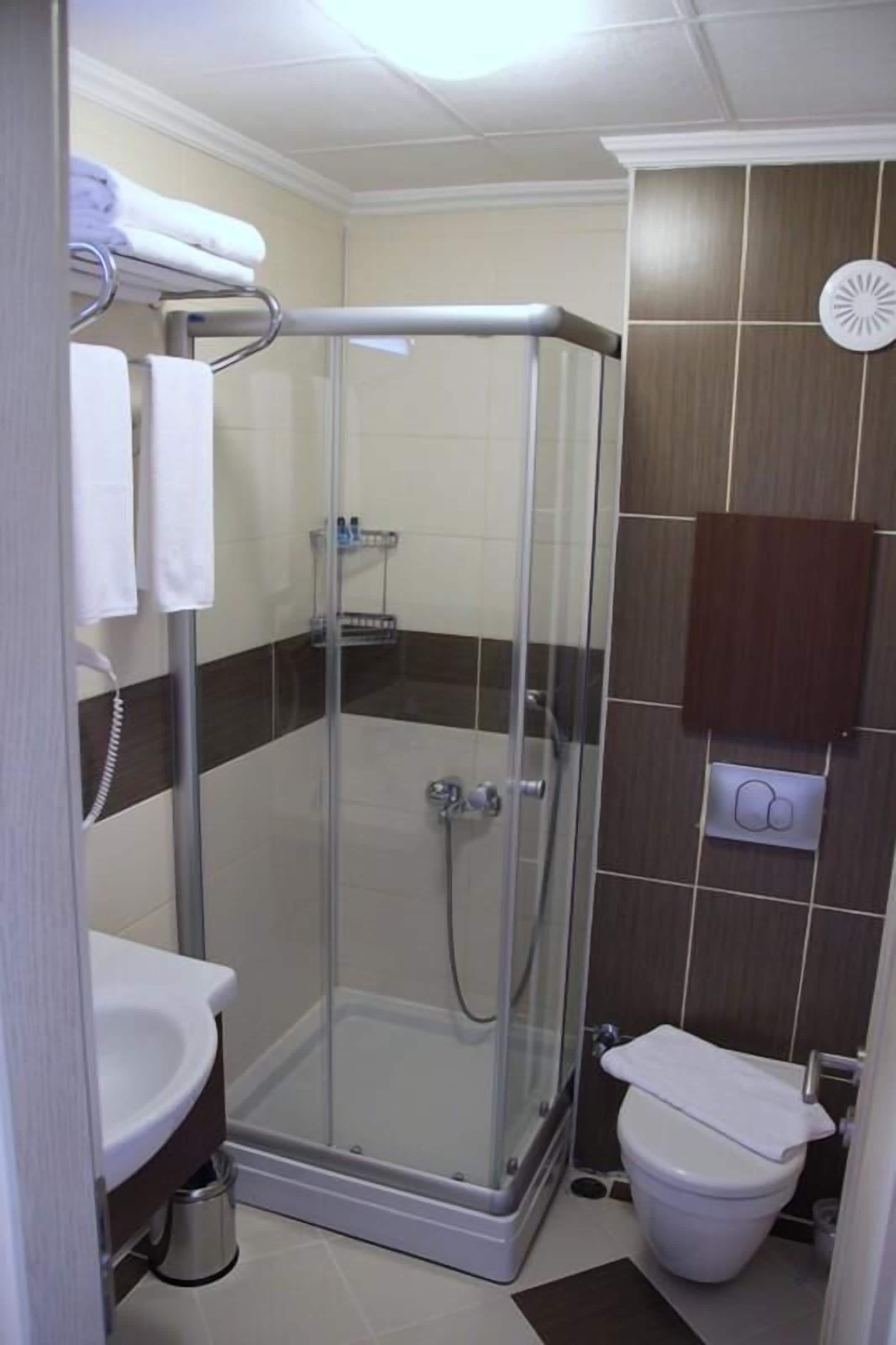 Een douchecabine met glazen deur, een wit wastafelmeubel en een toilet.