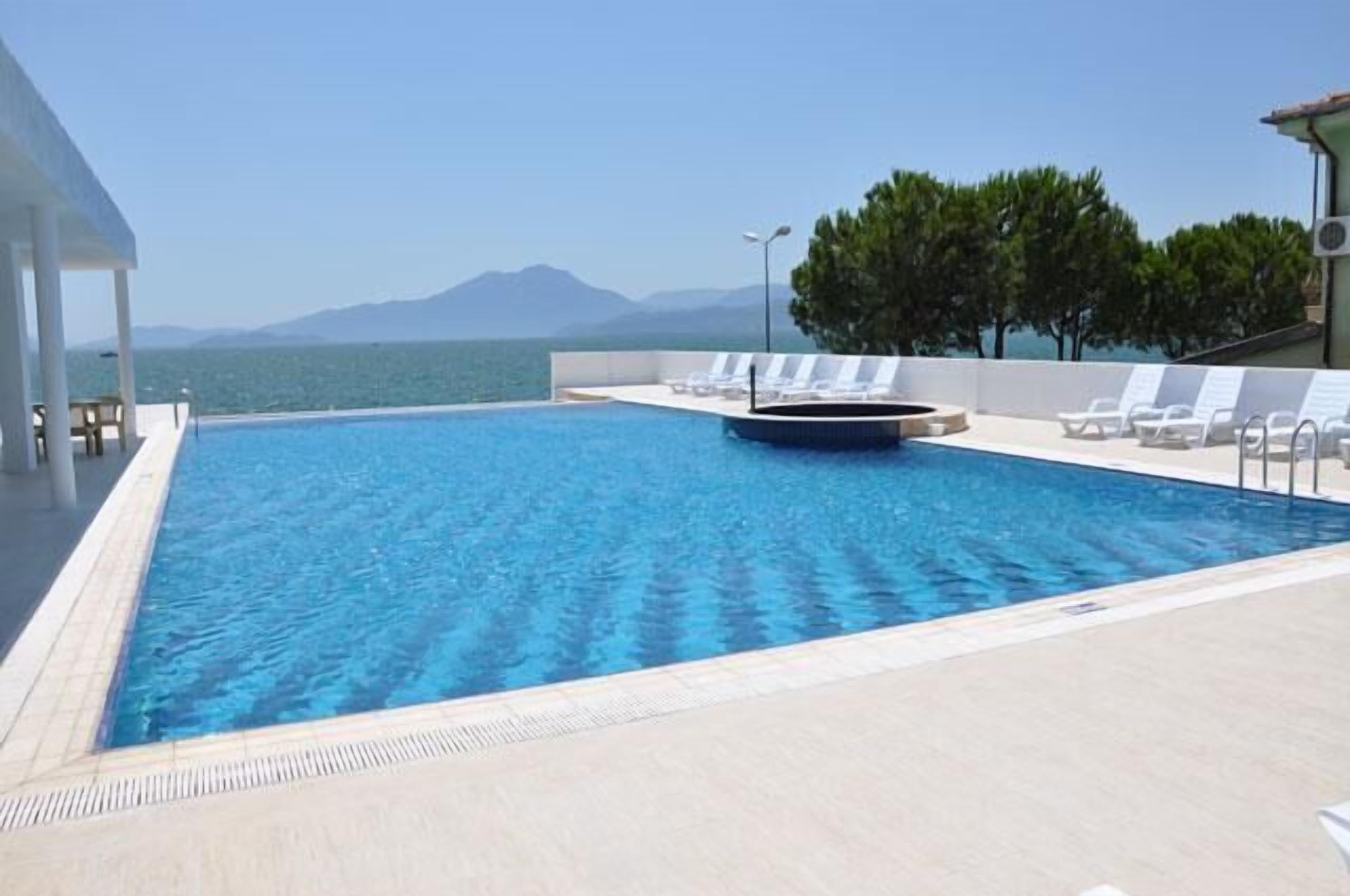 Piscina com vista para o mar e montanhas, rodeada por espreguiçadeiras e uma área coberta.