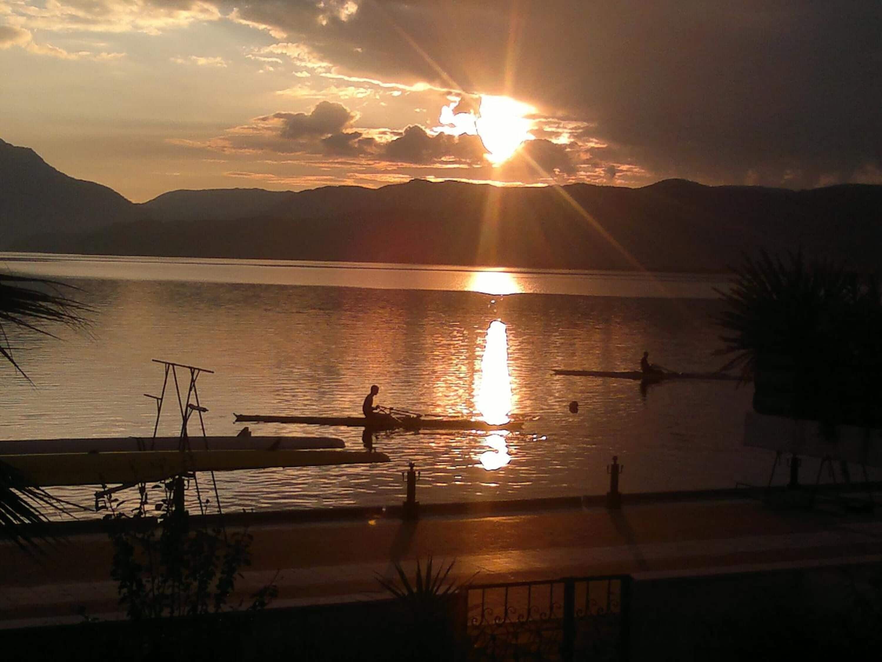 A sunset over a calm lake with boats and a dock.