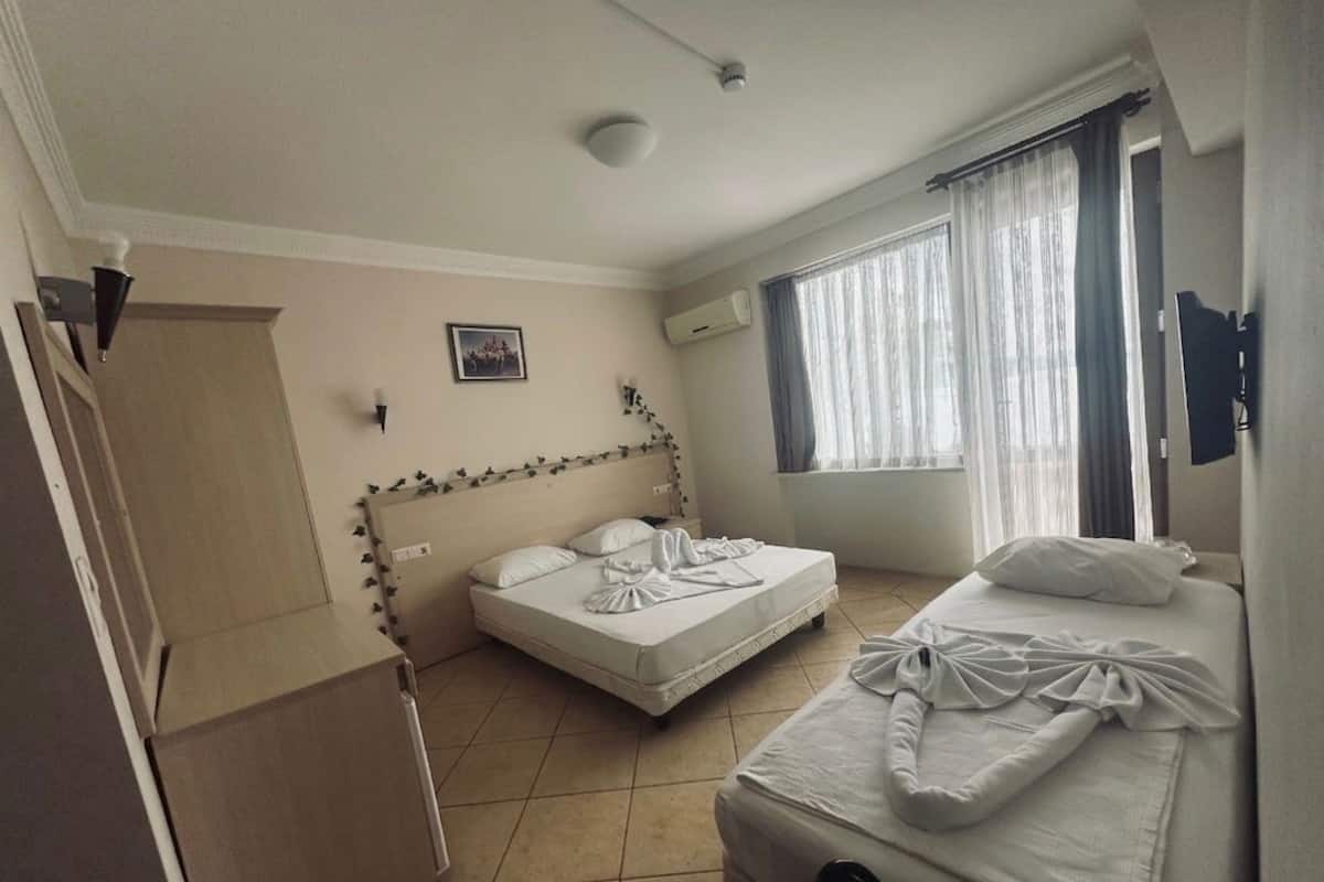 Une chambre d’hôtel avec deux lits, une fenêtre avec des rideaux, un appareil de climatisation et un tableau au mur.