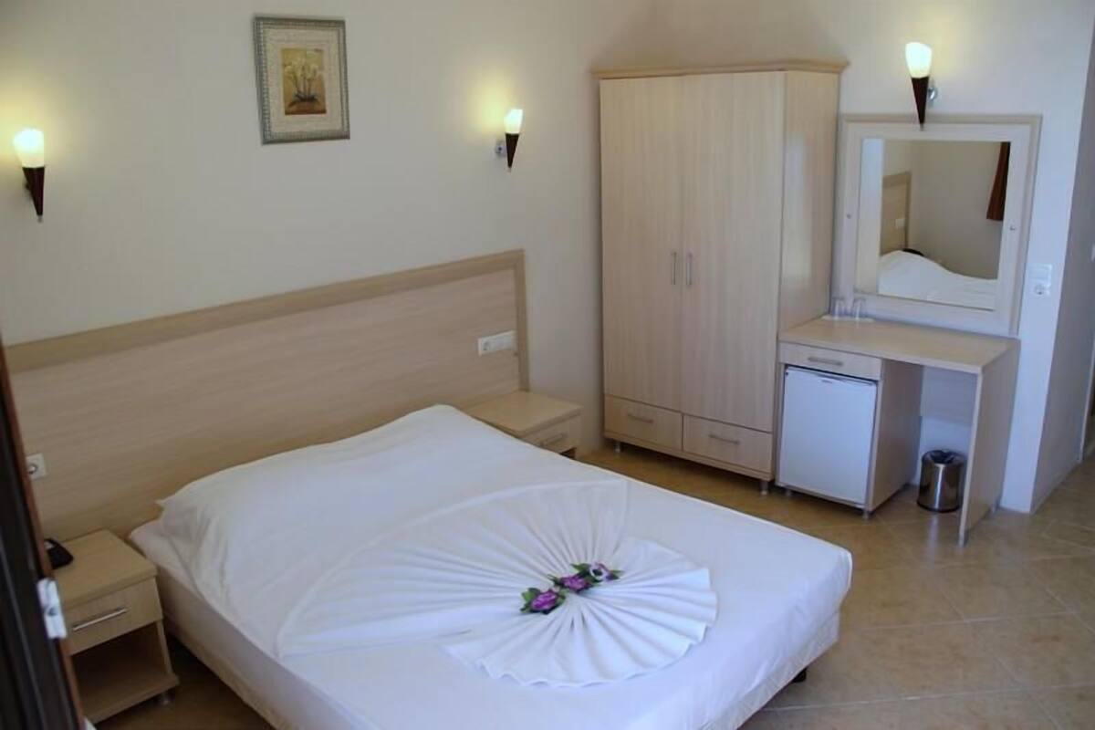 Une chambre d’hôtel comprenant un lit, une table de chevet, une armoire, un bureau avec un miroir et un petit réfrigérateur.