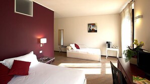 Habitación de hotel con dos camas, un escritorio, una silla, una mesita, una lámpara, un cuadro y una planta.