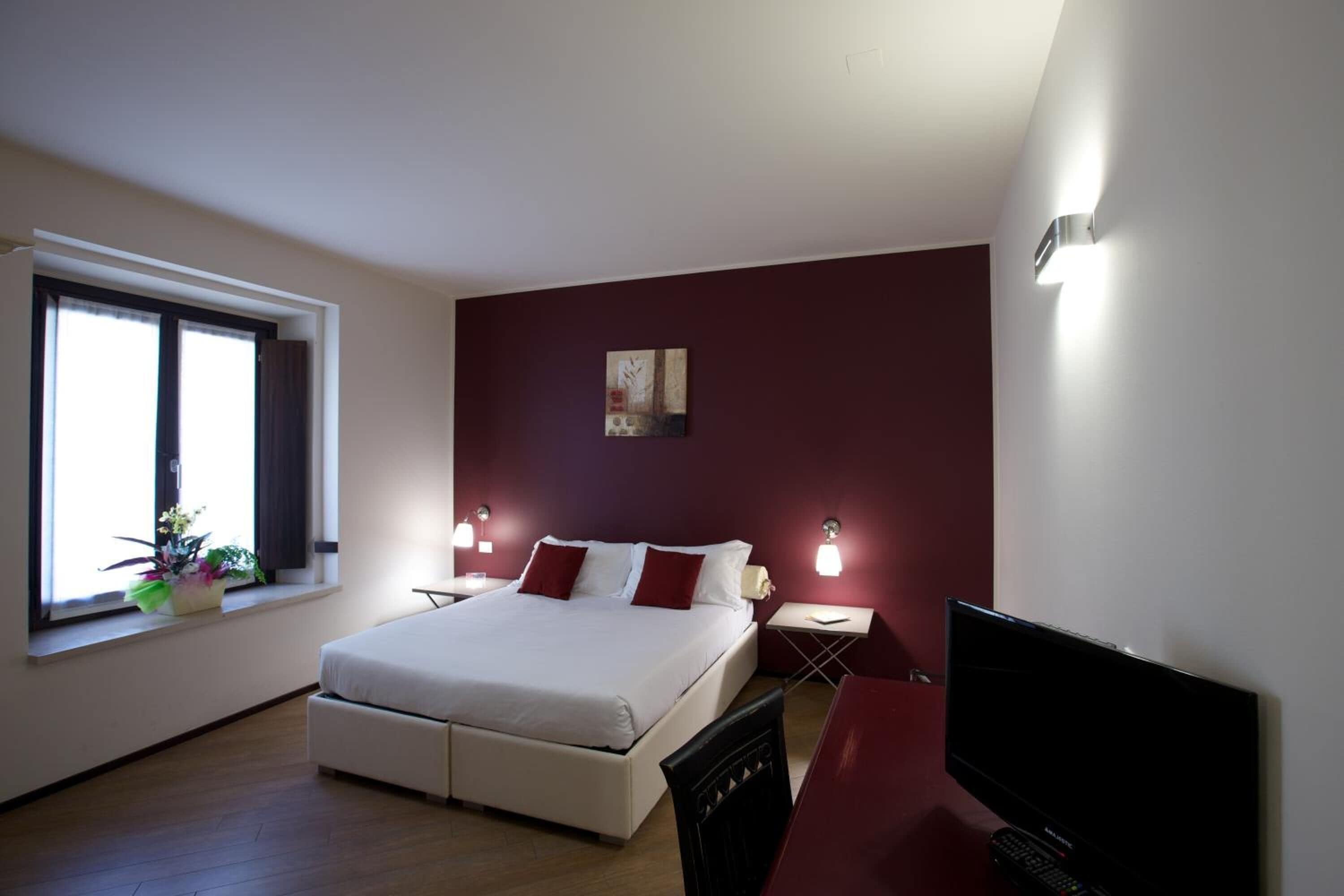 A bedroom with a bed, bedside tables, a desk, a television, and a window with curtains.