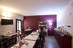A dining area with tables and chairs, a person using a laptop, and a buffet counter with food and drinks. - Hotel Leon D'Oro (Mantua)