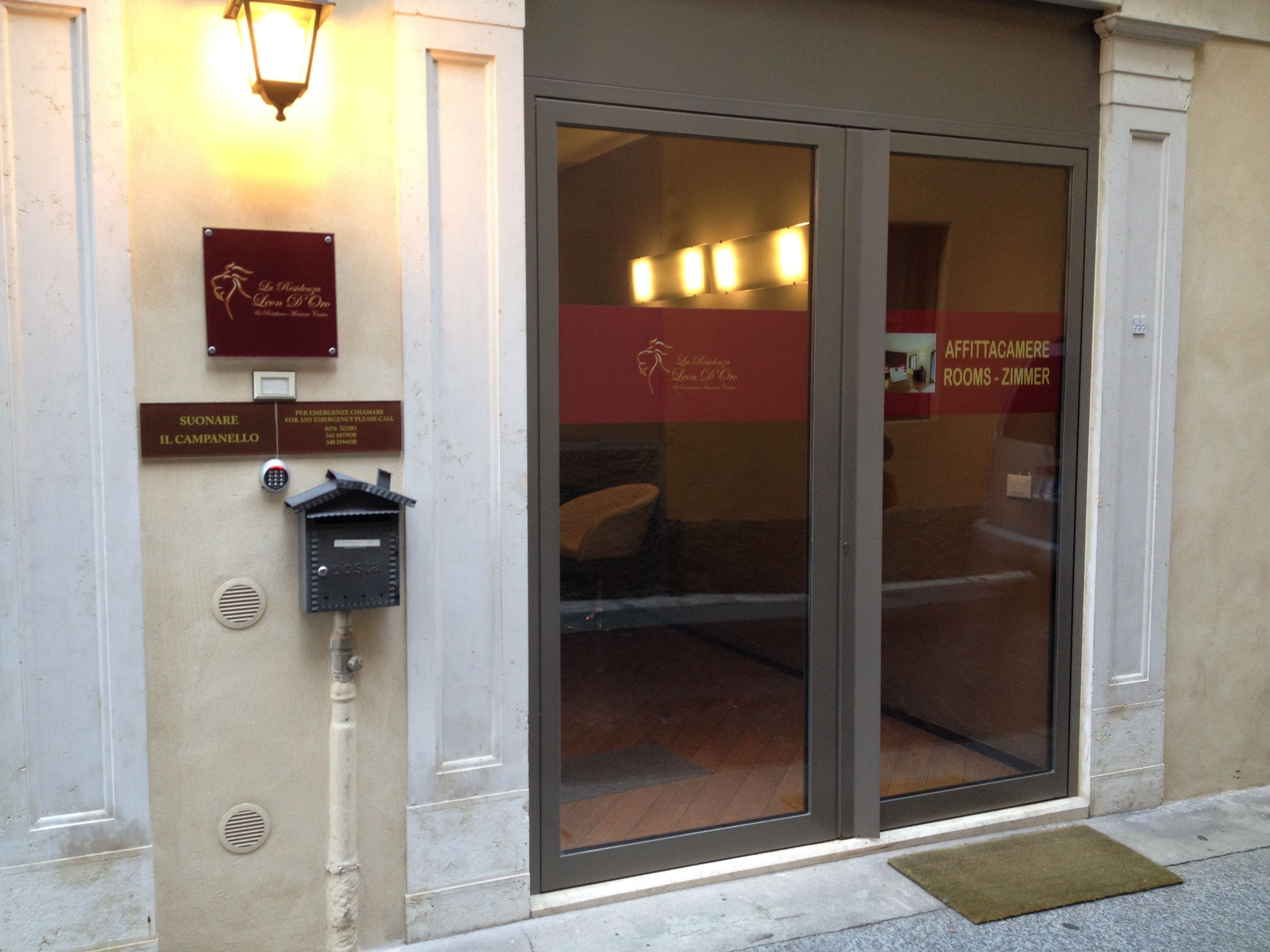 A hotel entrance with a glass door, emergency contact sign, and a room type sign.