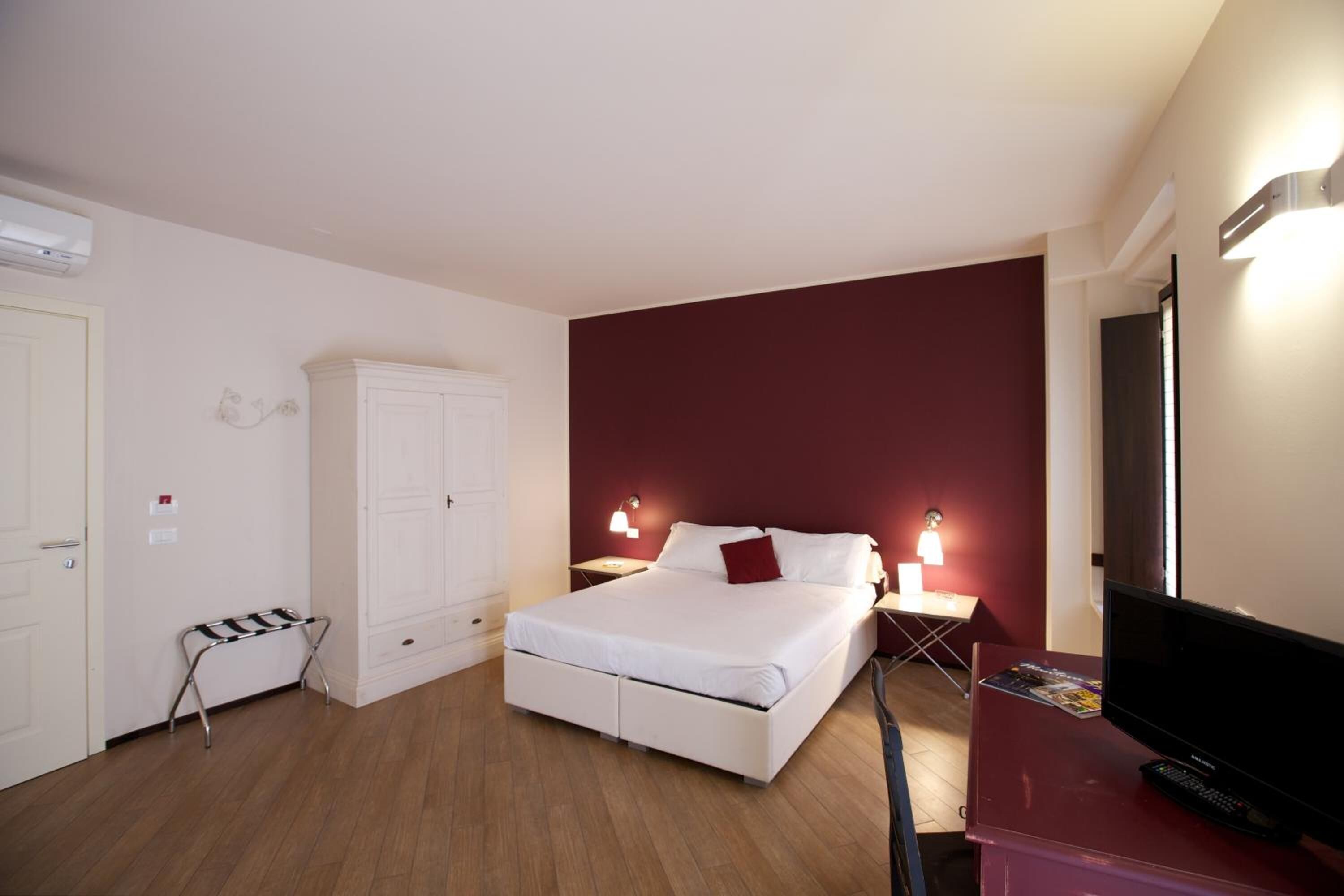 A hotel room with a bed, a wardrobe, a TV, and a small table with a lamp.