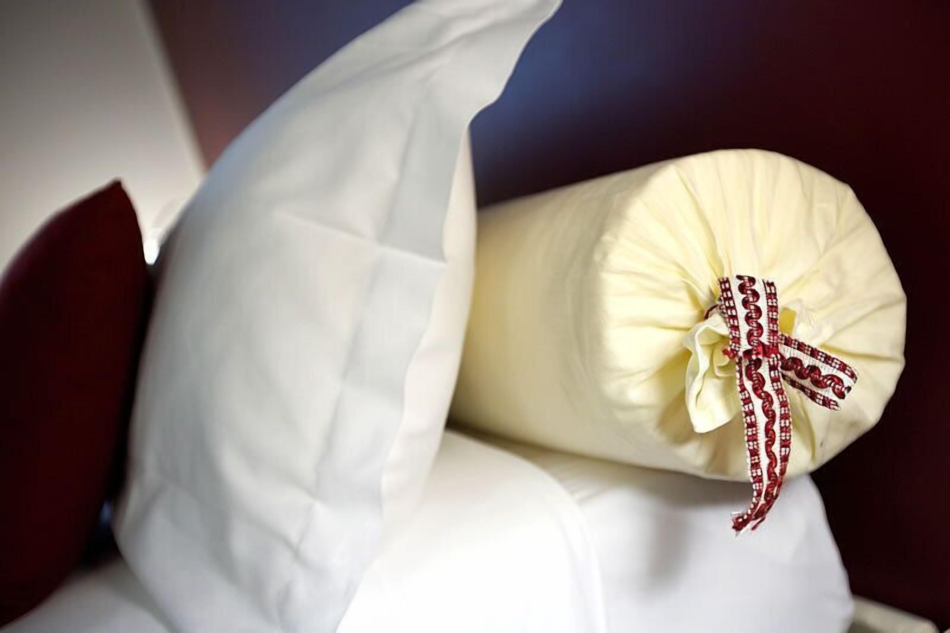 A pillow with a white cover and a red and white checkered ribbon tied around it.