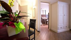 Una habitación con piso de madera, una silla negra, un armario blanco y una maceta con flores amarillas.