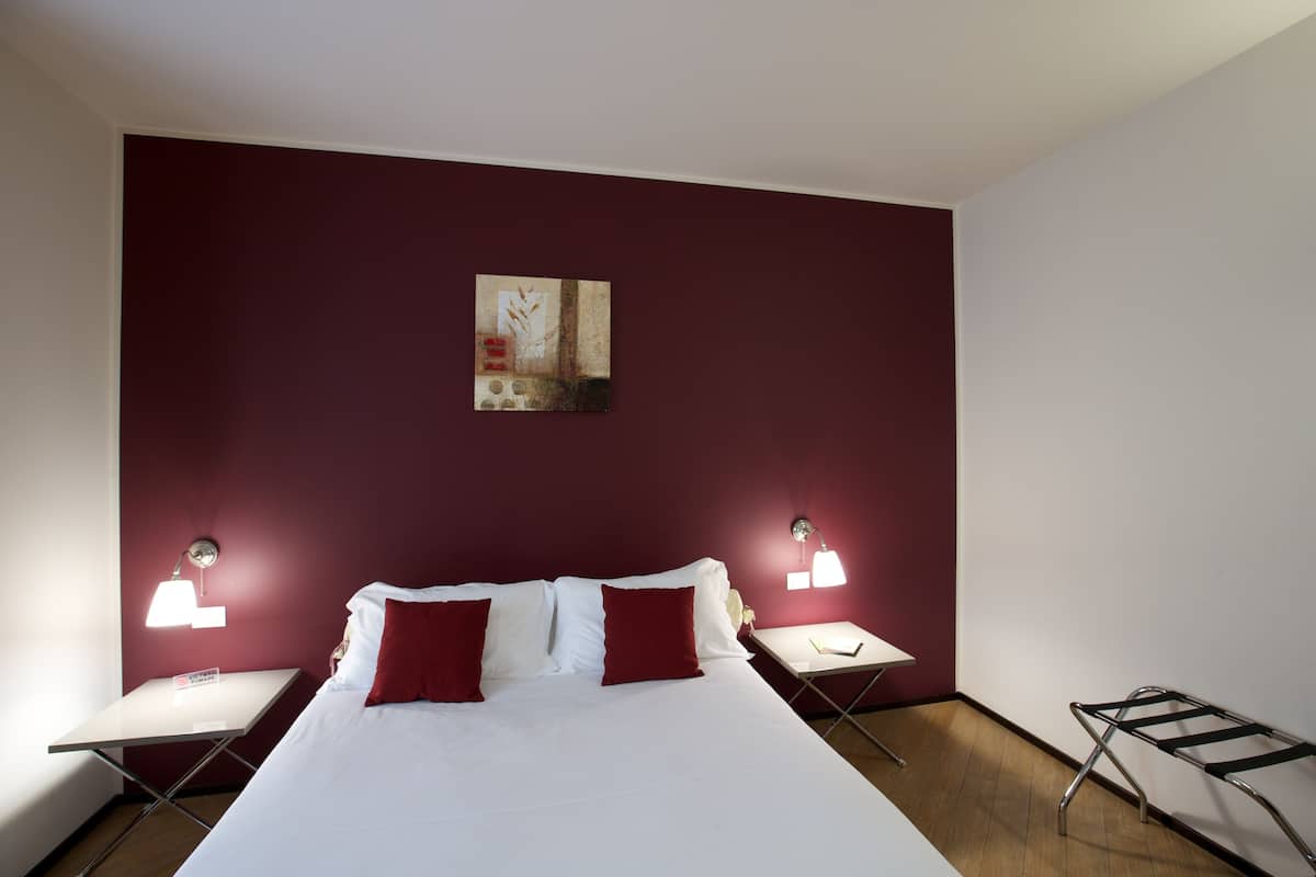 Une chambre d’hôtel avec un grand lit, deux tables de chevet, une œuvre d’art accrochée au mur et une lampe sur pied.