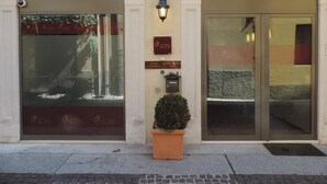Fachada de edificio con amplios ventanales, una planta en maceta y dos placas.