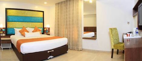 A hotel room with a large bed, a chair, a desk, a mirror, and a painting on the wall.