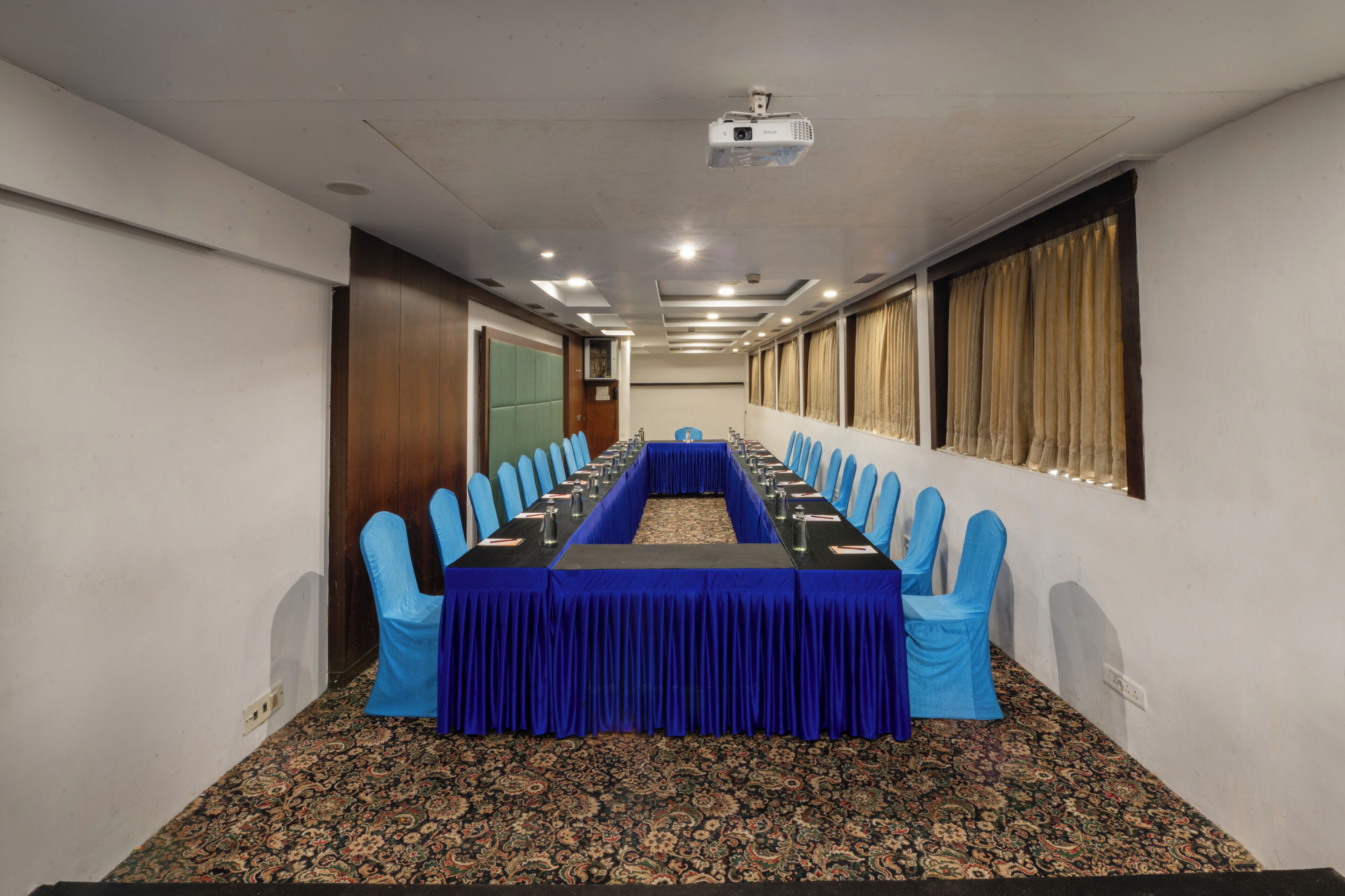 Un salón de conferencias con una larga mesa, sillas azules y suelo alfombrado.