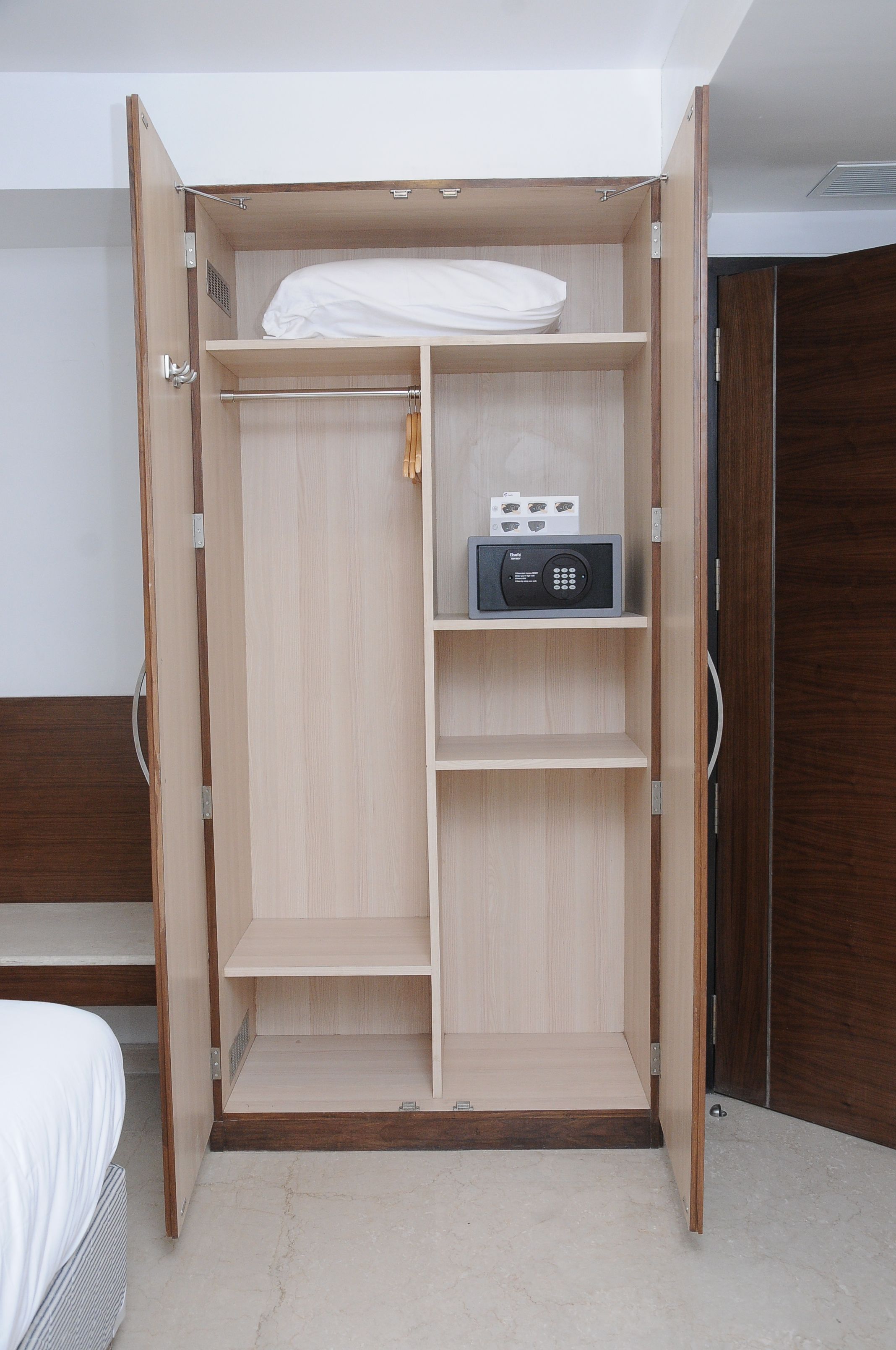 Un vestidor con terminación de madera, una barra para colgar ropa y un estante con un dispositivo electrónico negro.