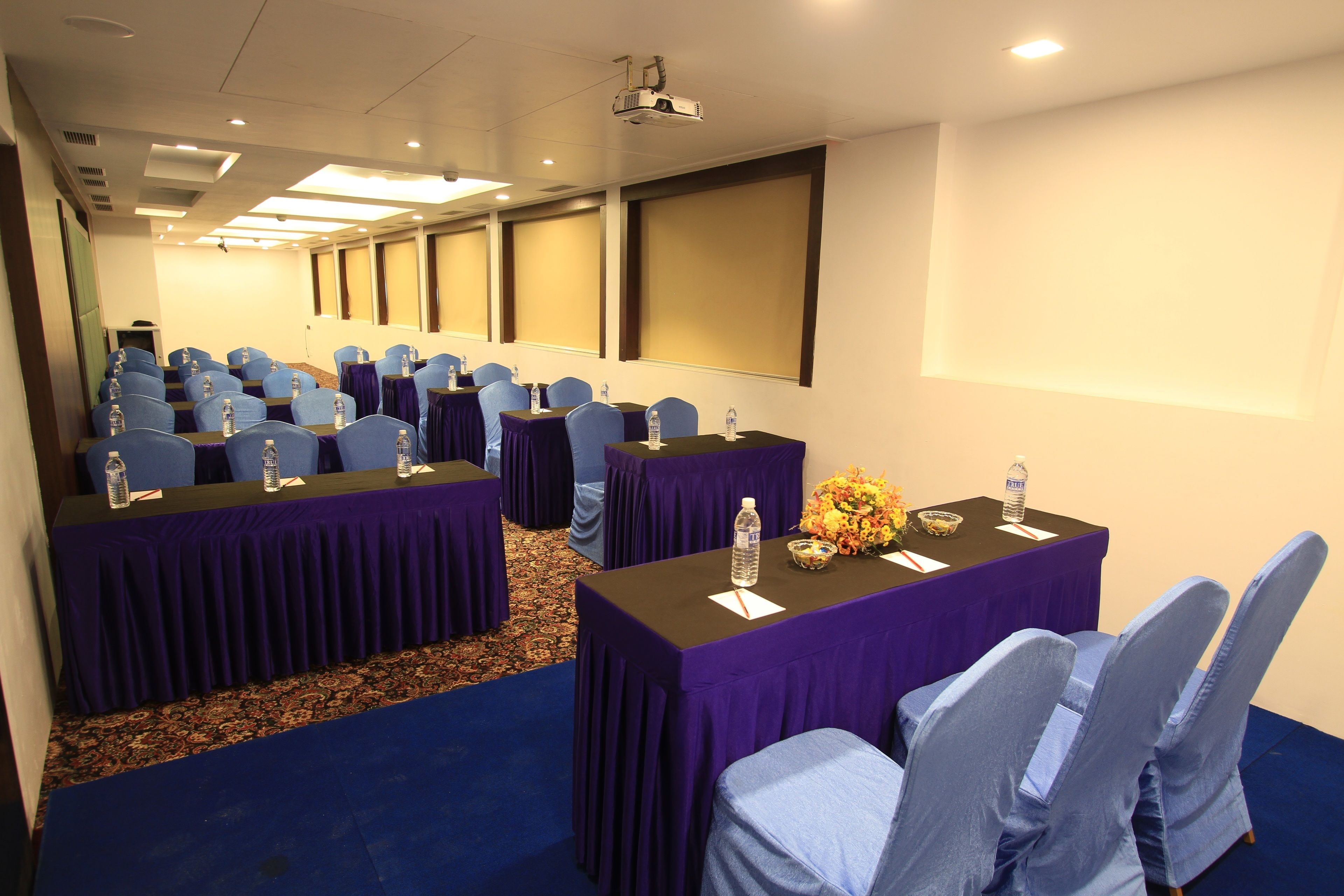 A conference room with rows of tables and chairs, equipped with water bottles and a projector.