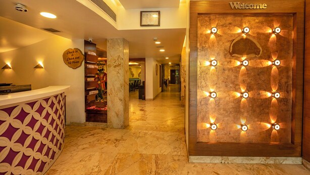 Zona de recepción de un hotel con piso de mármol, mostrador de recepción con diseño decorativo, un letrero que dice 'Welcome' e iluminación con lámparas en forma de abanico.