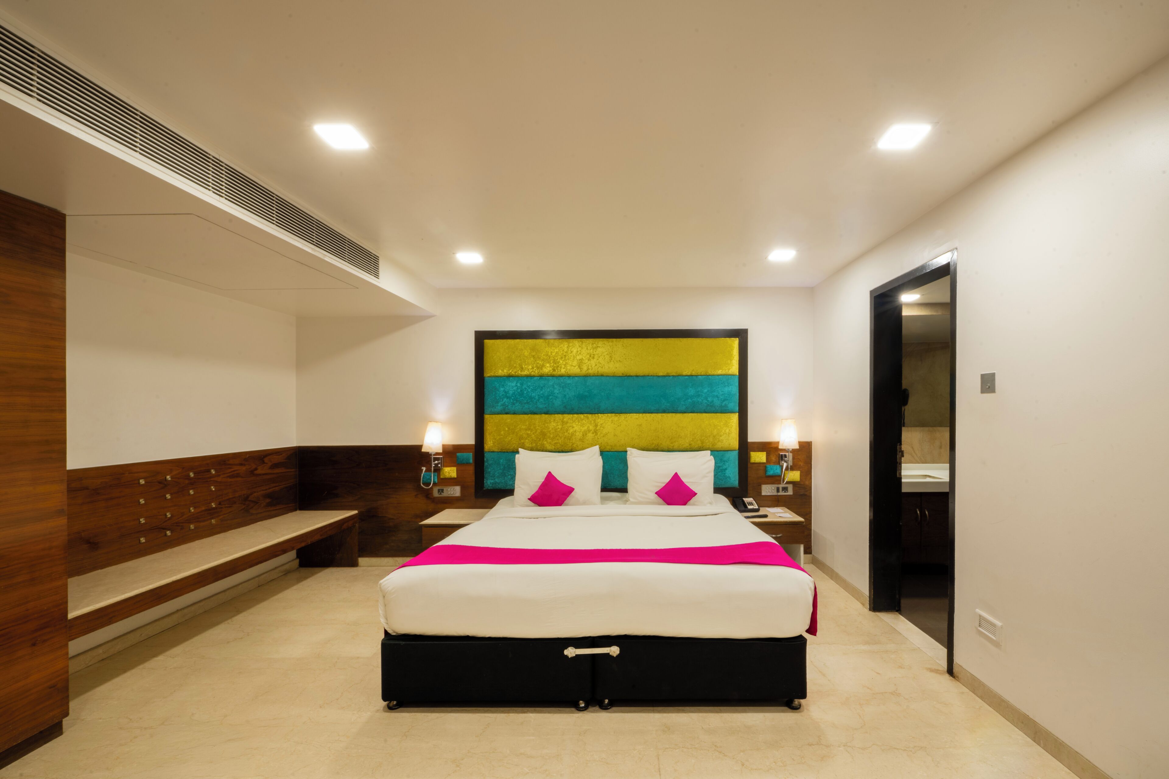 Una habitación de hotel moderna con una cama grande, un banco, una obra de arte en la pared y una puerta que da a otra habitación.