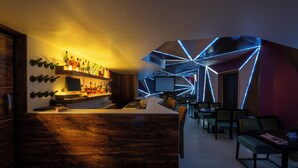 Una zona de bar con mostrador de madera, estantes llenos de botellas y un área de estar con mesas y sillas.