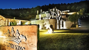 A sign for "Golden King Luxury Resort" with a stone facade and a view of a modern building with multiple levels and a staircase leading to a balcony. - Golden King (Skiathos)