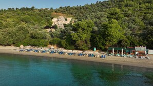 A beach with rows of sun loungers and umbrellas, a building in the background, and a clear view of the sea. - Golden King (Skiathos)