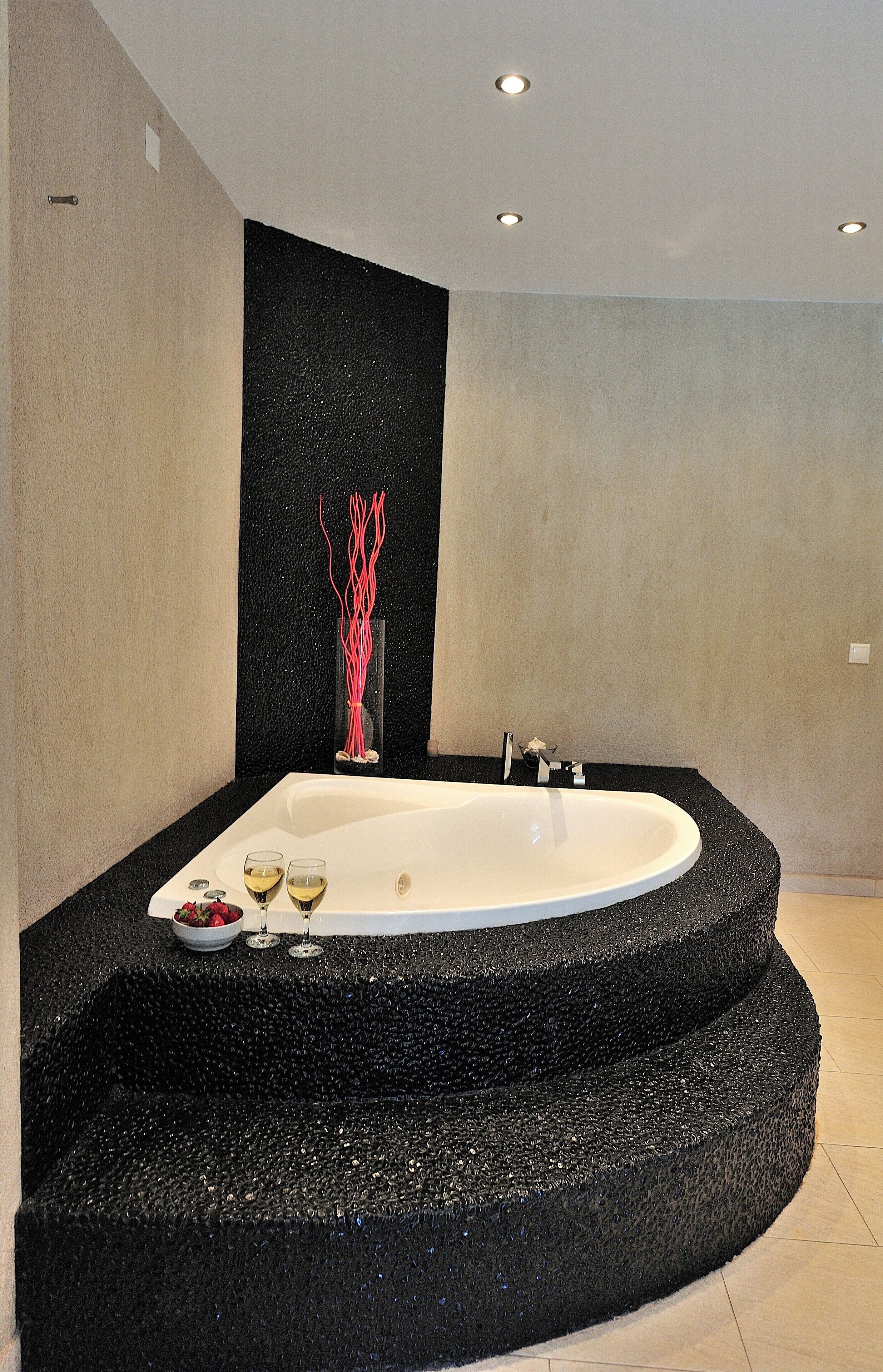 Ein modernes Badezimmer mit einer freistehenden Badewanne, einer Wand mit schwarzer Struktur und einer dekorativen Vase mit roten Ästen.