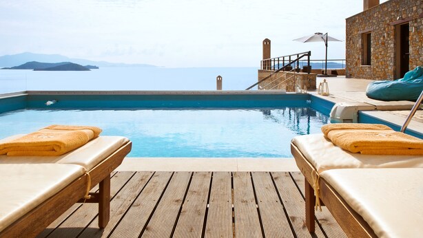 A poolside area with two sun loungers, a stone building, and a view of the sea. - Golden King (Skiathos)