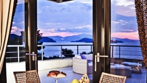 A dining table with a fruit bowl and a glass of wine, overlooking a scenic view of mountains and water. - Golden King (Skiathos)
