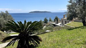 A coastal landscape with a clear view of the sea, a small island in the distance, and a building with a stone facade. - Golden King (Skiathos)