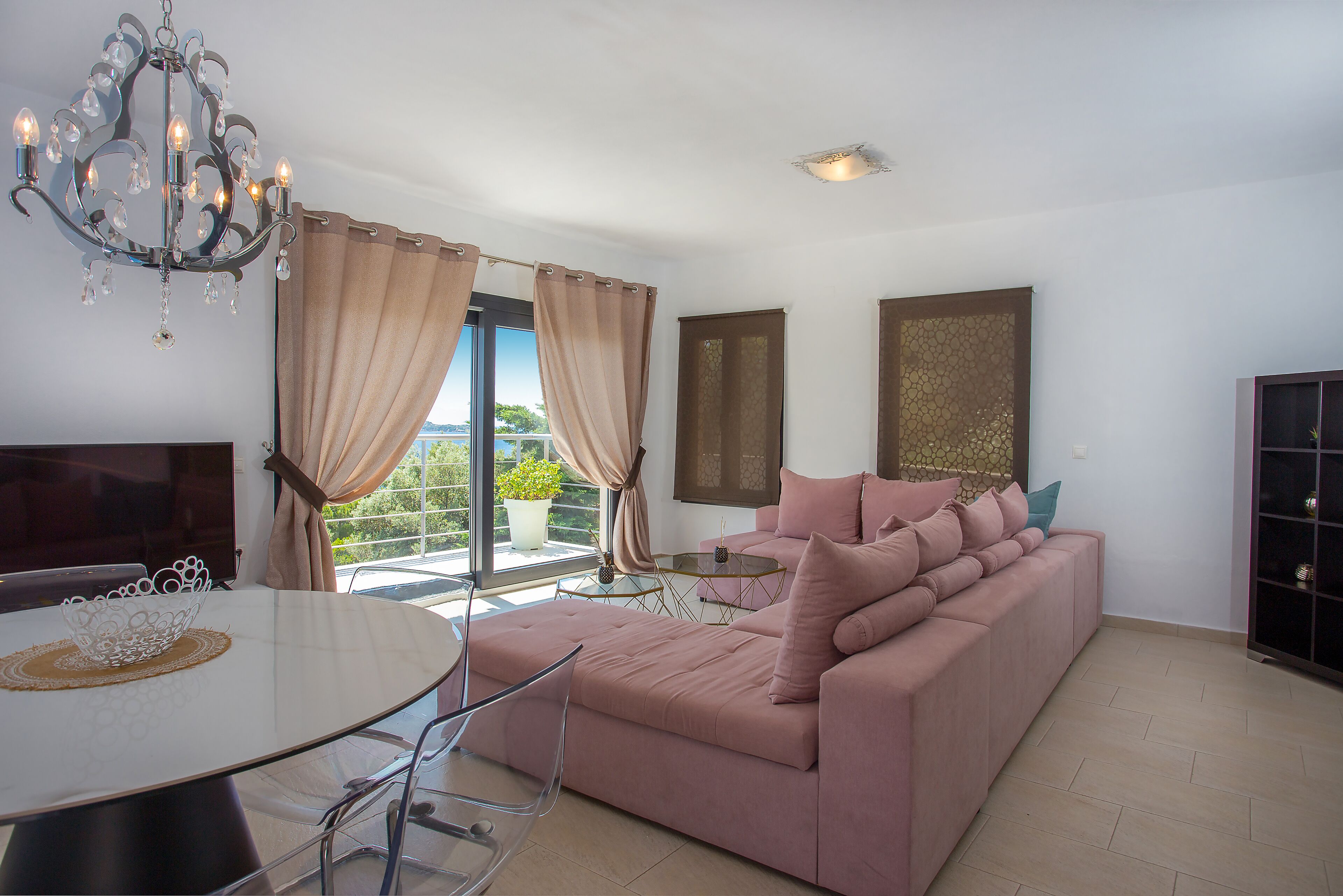 A modern living room with a pink sofa, a glass dining table, and a chandelier.