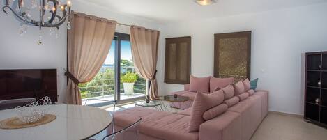 A modern living room with a pink sofa, a glass dining table, and a chandelier.