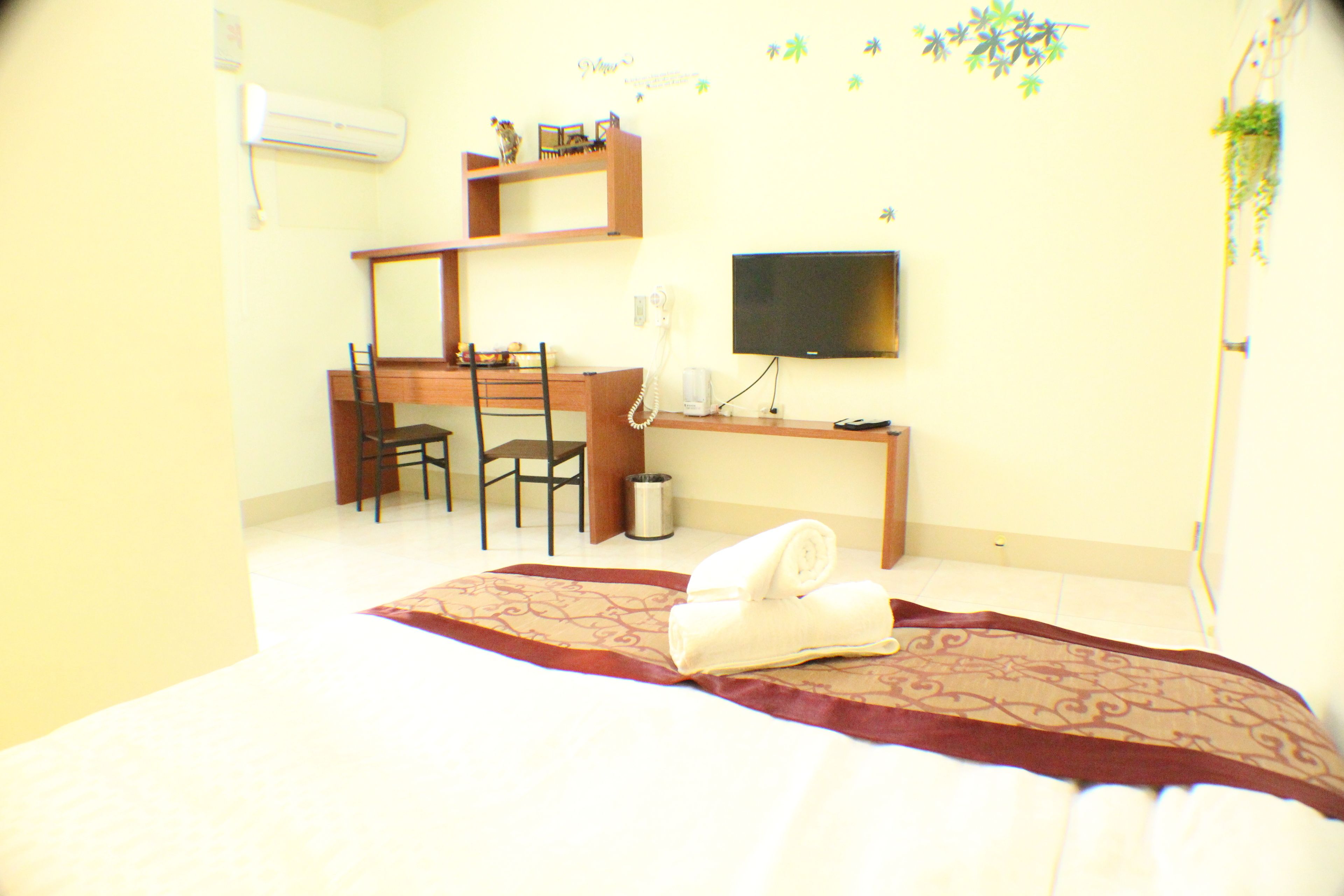A hotel room with a bed, a desk with a chair, a television, and a small plant.