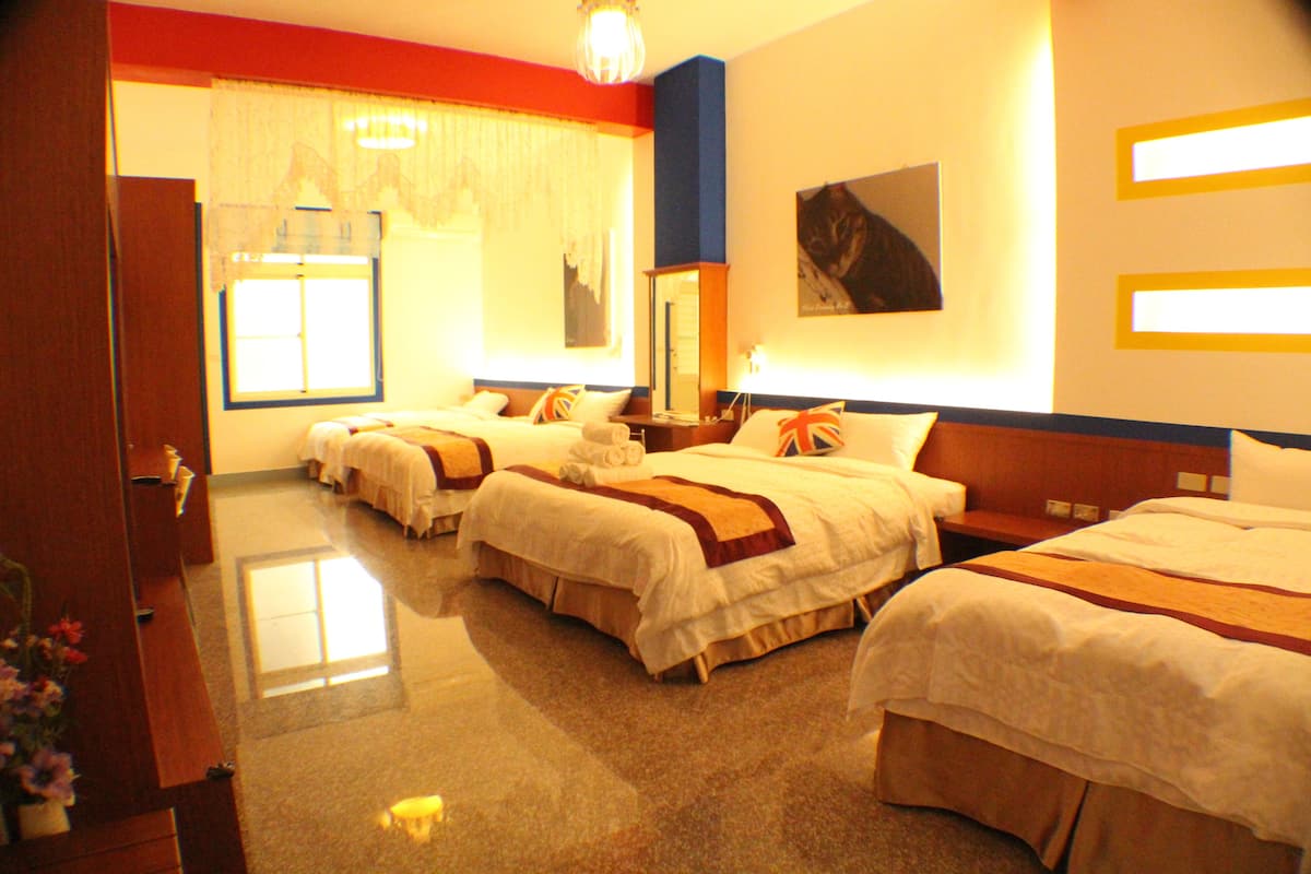 Habitación de hotel con tres camas, un ventanal con cortinas, un candelabro y un cuadro en la pared.