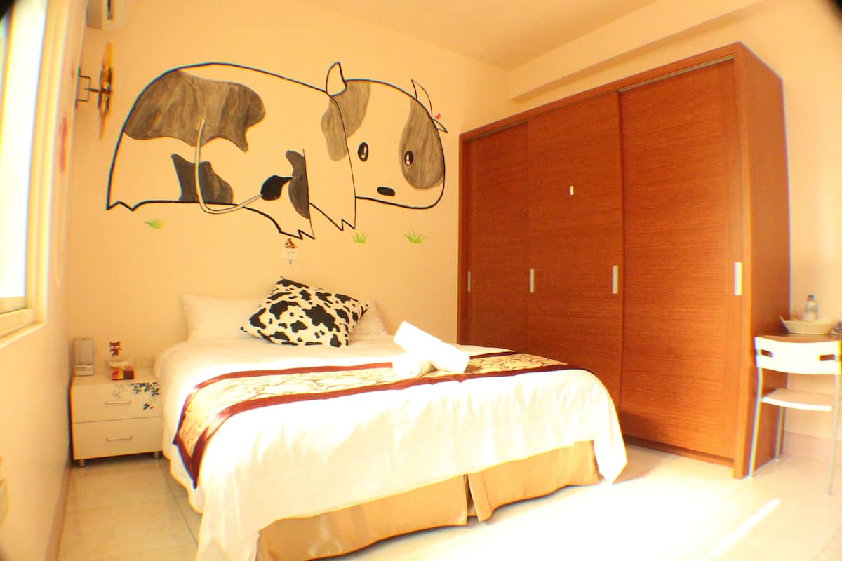 Un dormitorio con cama, armario de madera, mesita de noche y un mural en la pared.
