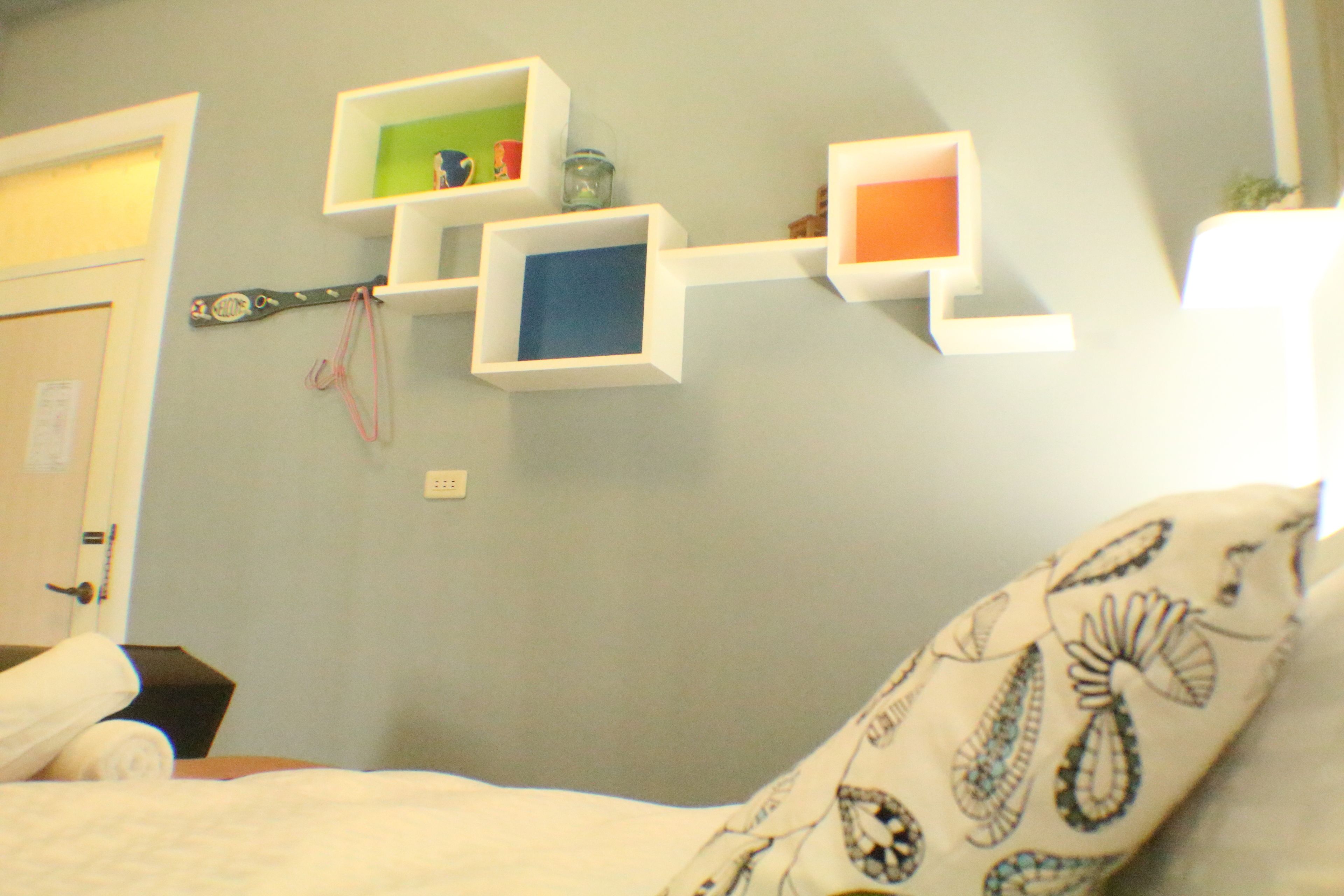 A bedroom with a bed, a pillow with a paisley pattern, and wall-mounted shelves with various items.