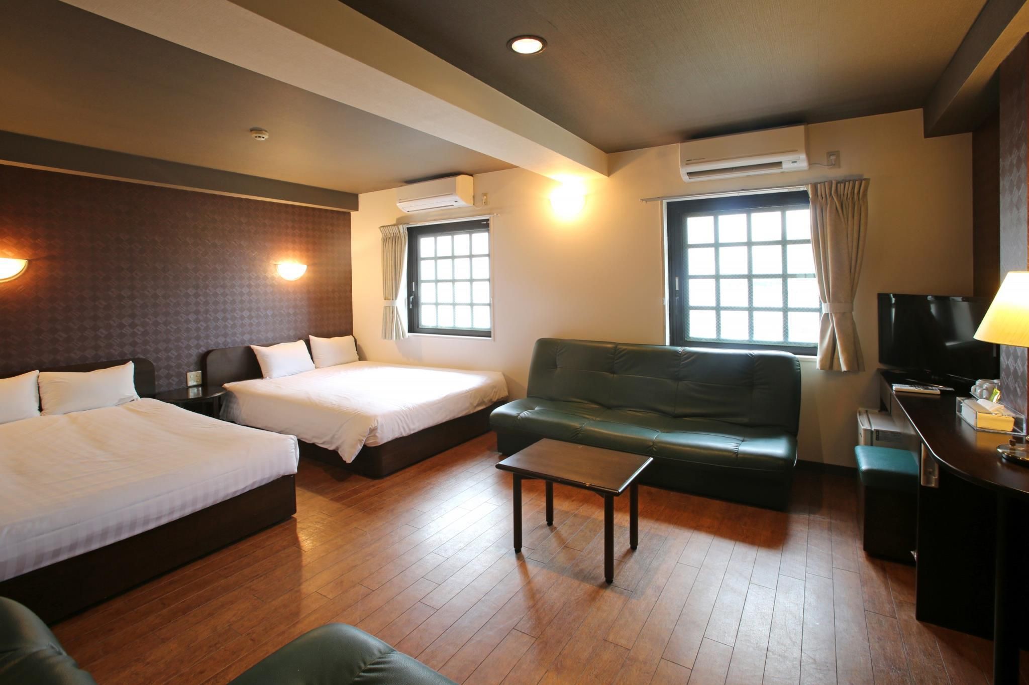 A hotel room with two beds, a sofa, a TV, and a desk.
