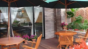 An outdoor patio area with wooden furniture, including tables and chairs, and a large umbrella providing shade.
